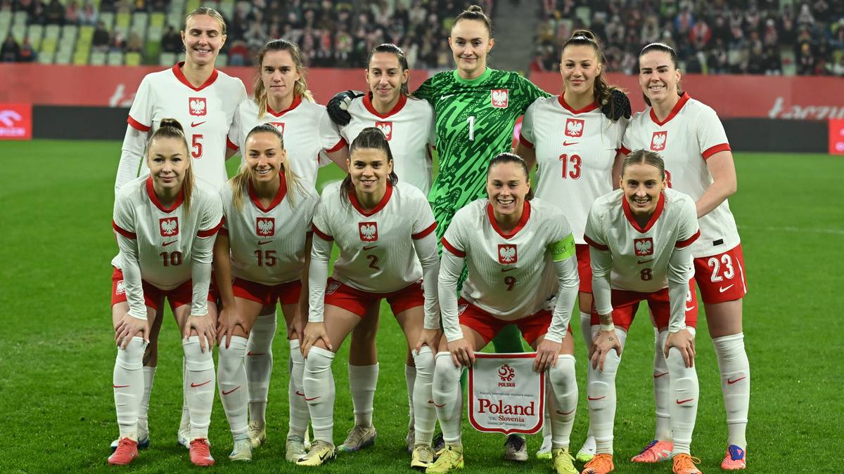 Drużyna piłkarska kobiet Polski w białych strojach, pozująca do zdjęcia na boisku.