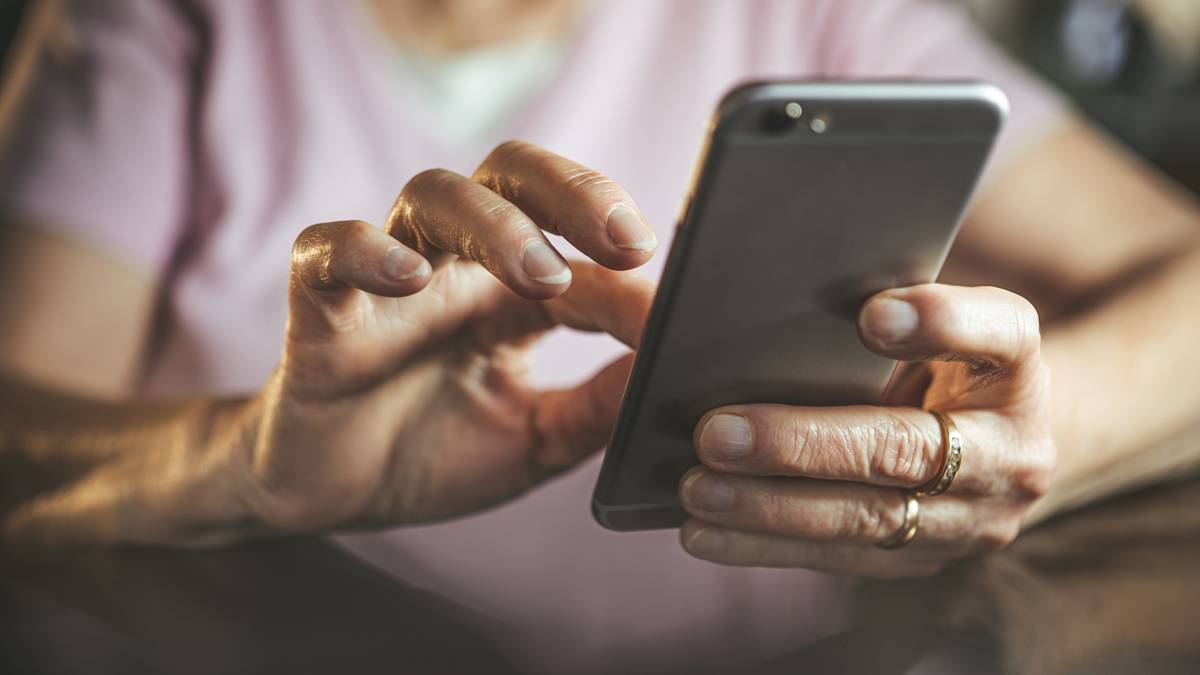 Zbliżenie na dłonie osoby korzystającej ze smartfona, palce dotykają ekranu.