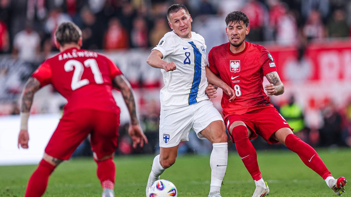 Piłkarze reprezentacji Polski walczą o piłkę z przeciwnikiem w białym stroju.