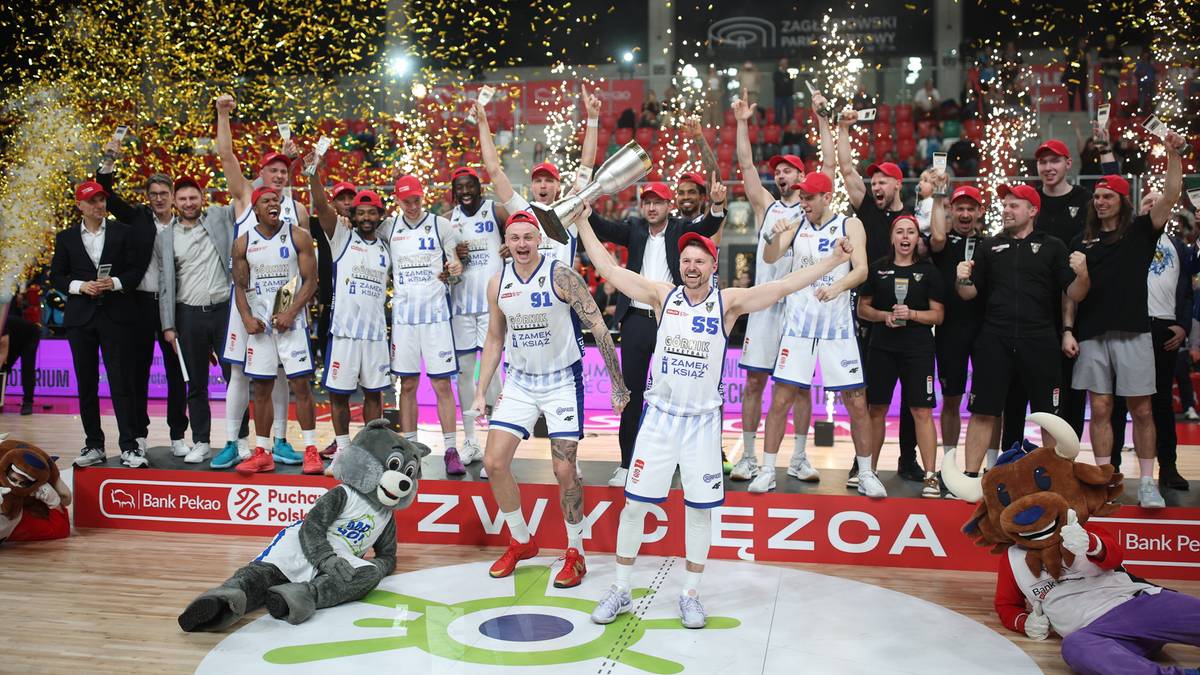 Drużyna koszykarzy w białych strojach świętuje zwycięstwo, unosząc trofeum w powietrze, podczas gdy sypie się złote konfetti.