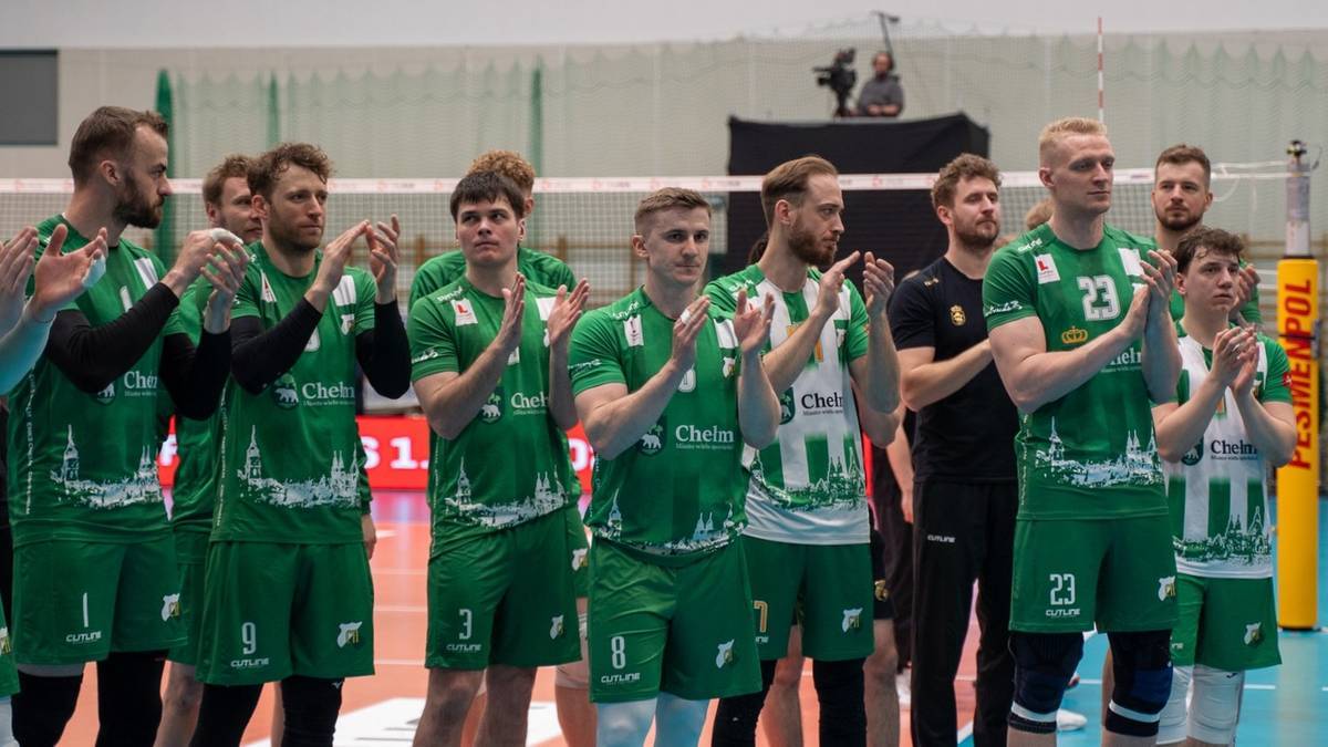 Grupa zawodników siatkówki w zielonych strojach stoi w rzędzie, trzymając ręce złożone w geście aplauzu lub pożegnania.