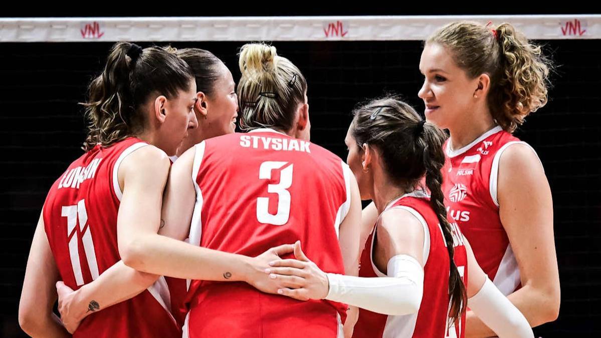 Drużyna siatkarek w czerwonych strojach z białymi napisami, stojąca w k&oacute;łku i przytulająca się przed meczem.