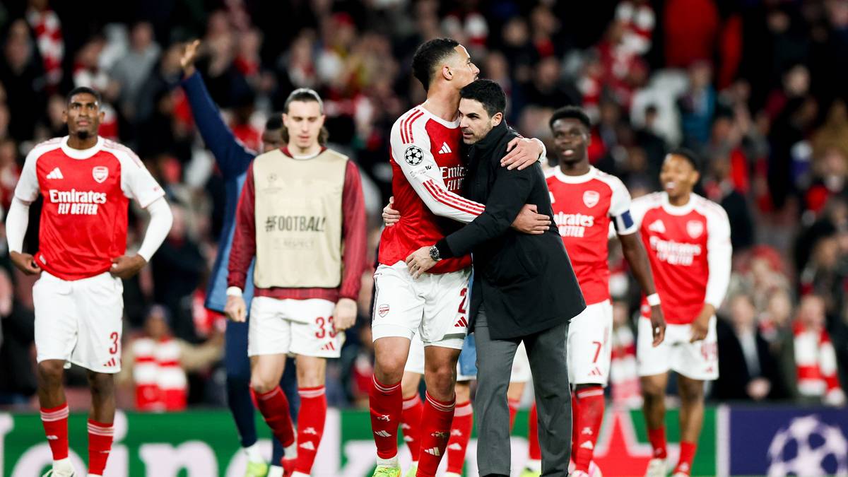 Piłkarze Arsenalu w czerwonych strojach na murawie, jeden z nich jest przytulany przez mężczyznę w garniturze.