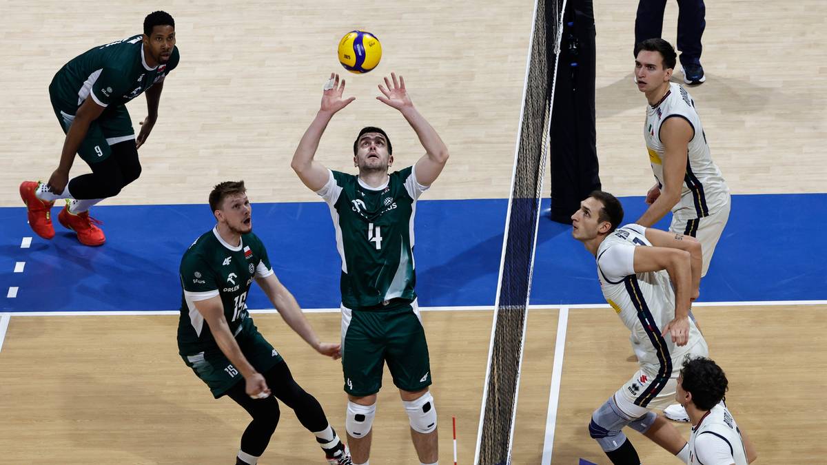 Siatkarze w akcji podczas meczu, jeden z nich zagrywa piłkę nad siatką.