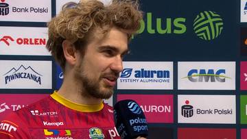 Portret Jakuba Popiwczaka, zawodnika piłki ręcznej, mówiącego do mikrofonu, z logotypami sponsorów w tle.