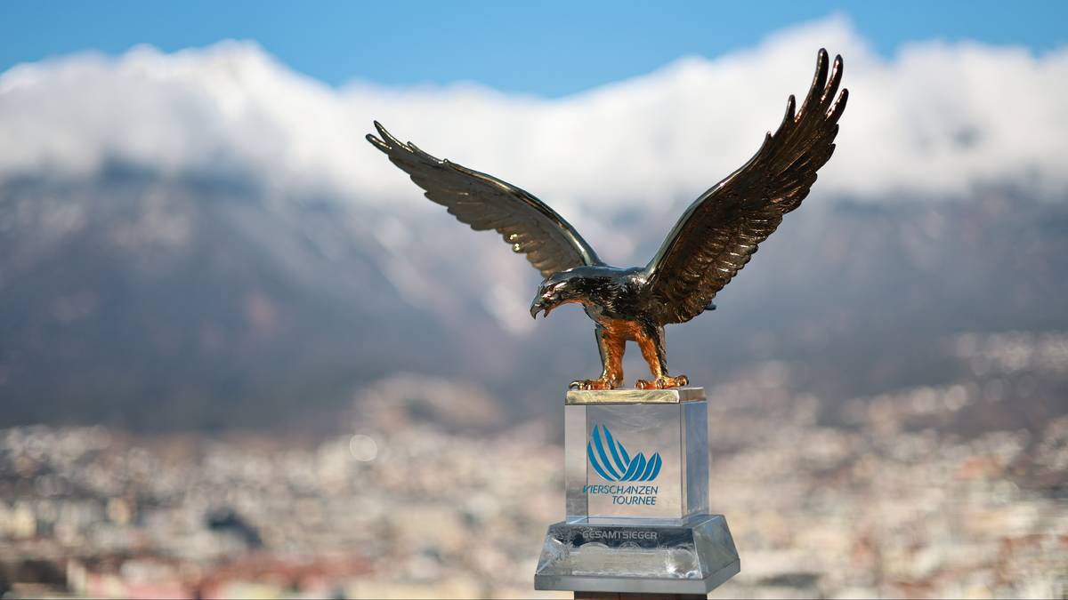 Statuetka orła na cokole, symbol Turnieju Czterech Skoczni, na tle g&oacute;r i błękitnego nieba.