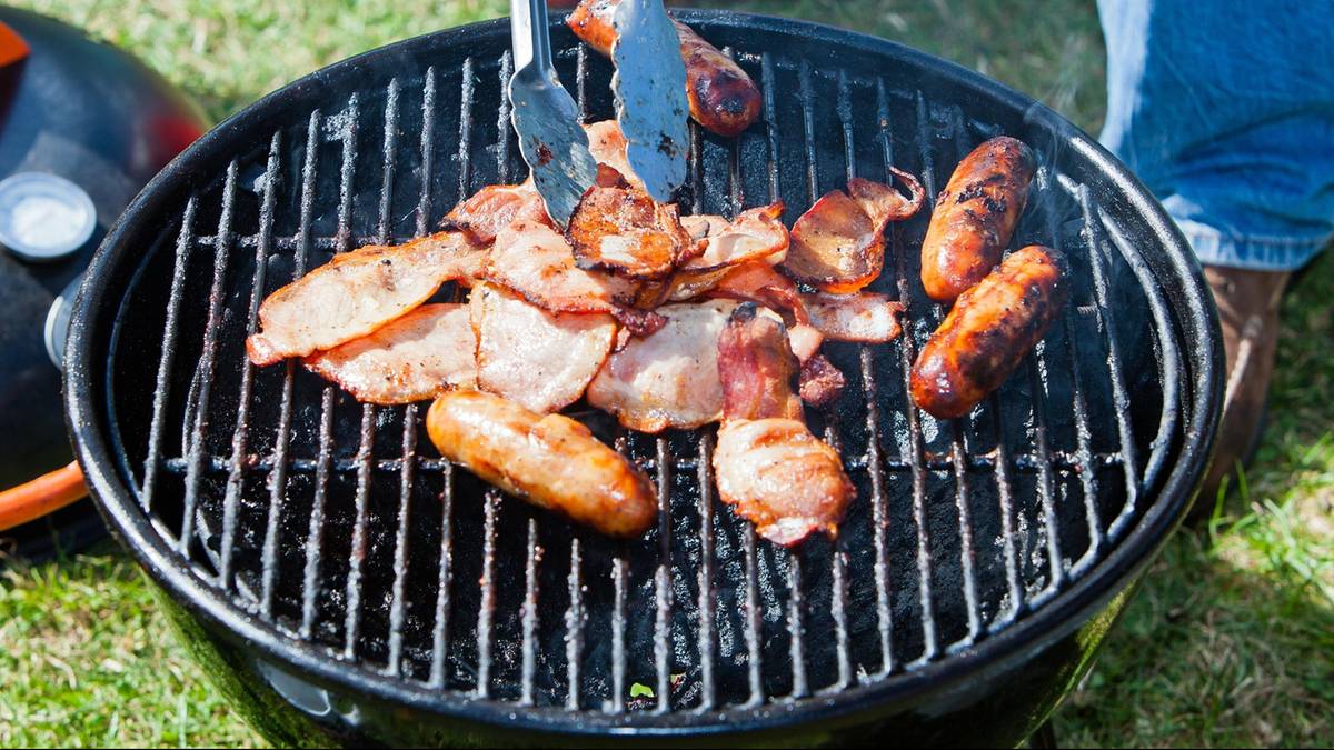 Mięso na grillu, w tym kiełbaski i boczek, obracane szczypcami na ruszcie.