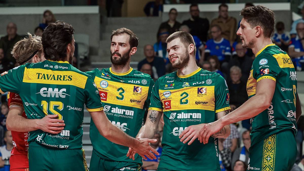 Czterech siatkarzy Aluron CMC Warty Zawiercie w zielono-ż&oacute;łtych strojach, z numerami na plecach, stojący razem na boisku.