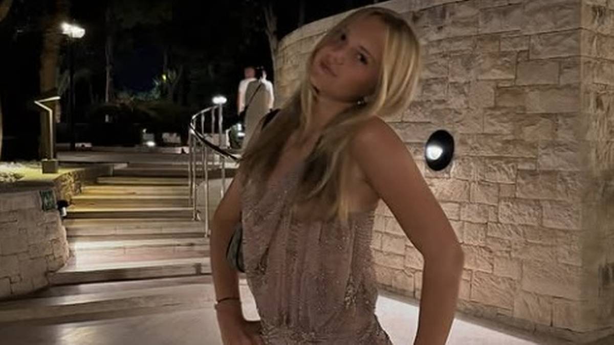 Młoda kobieta z długimi blond włosami w kr&oacute;tkiej sukience, pozująca z rękami na biodrach.