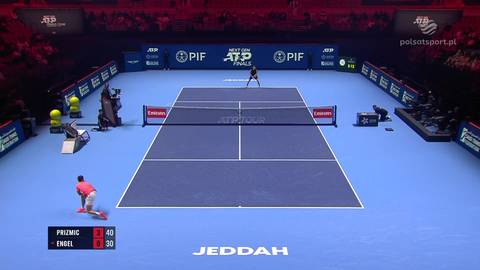 Dw&oacute;ch tenisist&oacute;w grających mecz na korcie tenisowym, jeden przy siatce, drugi na linii końcowej. Wynik meczu wyświetlany na tablicy.