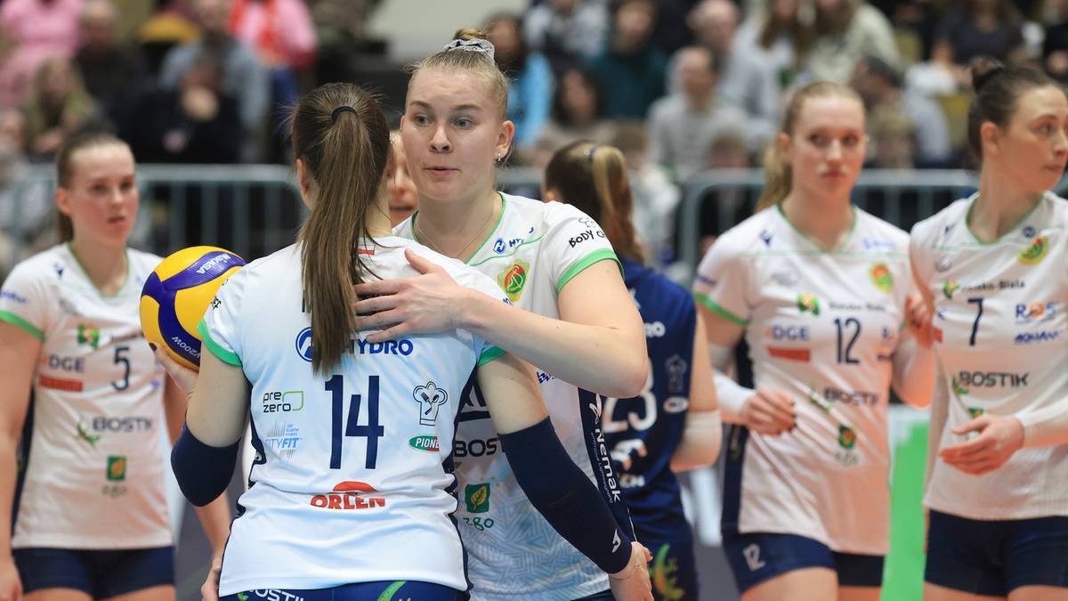 Siatkarki BKS Bostik Bielsko-Biała w białych strojach, jedna z nich obejmuje drugą. W tle inne zawodniczki i kibice.