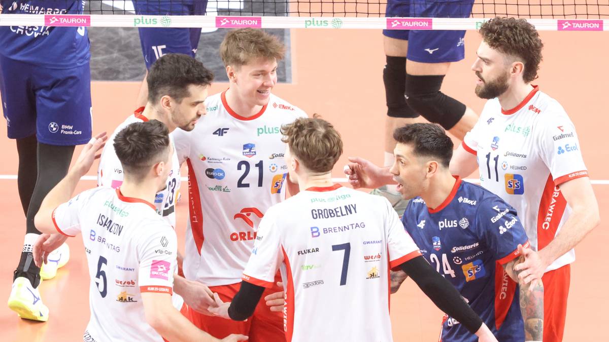 Grupa siatkarzy ZAKSY Kędzierzyn-Koźle w strojach sportowych, kilku z nich przybija sobie piątkę, podczas rozmowy na boisku.