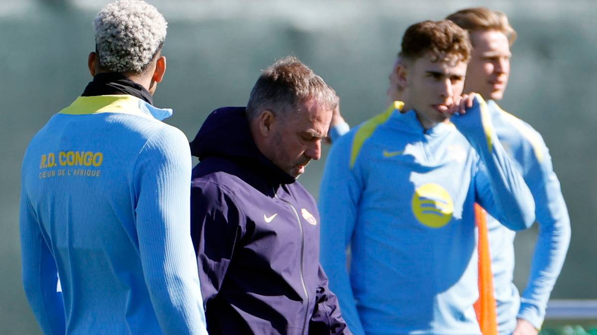 Trzech mężczyzn w strojach sportowych rozmawia na boisku piłkarskim.