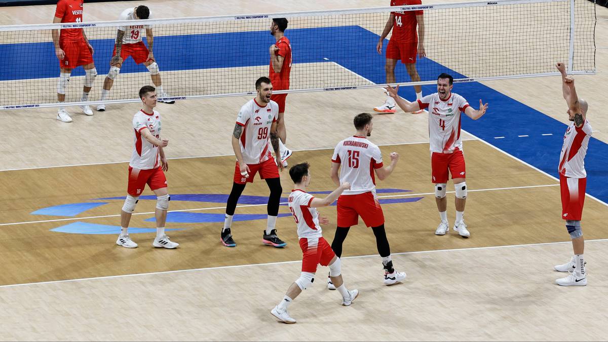 Drużyna siatkarzy w czerwono-białych strojach gra na boisku, jeden z zawodników podnosi ręce w geście radości.