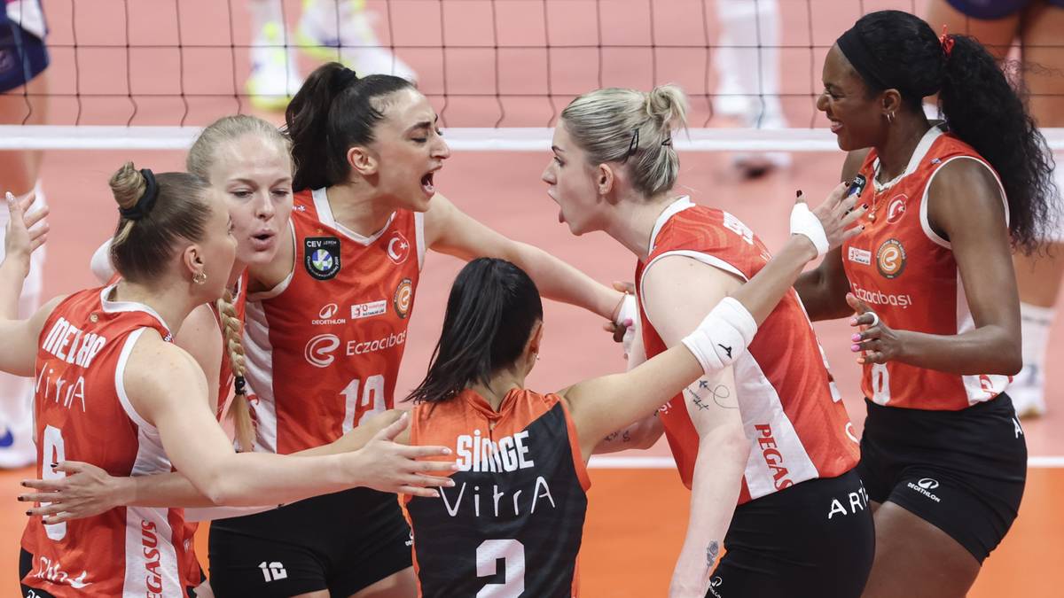 Grupa siatkarek w pomarańczowych strojach świętuje zdobycie punktu, przytulając się i rozmawiając.