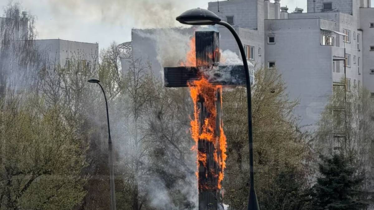 Drewniany krzyż, obity blachą, płonie z widocznym dymem i płomieniami.