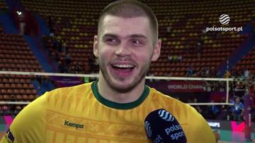 Młody mężczyzna, prawdopodobnie siatkarz, w ż&oacute;łtej koszulce z zielonym kołnierzykiem, uśmiecha się szeroko do kamery. Trzyma w ręku mikrofon z logo Polsat Sport.