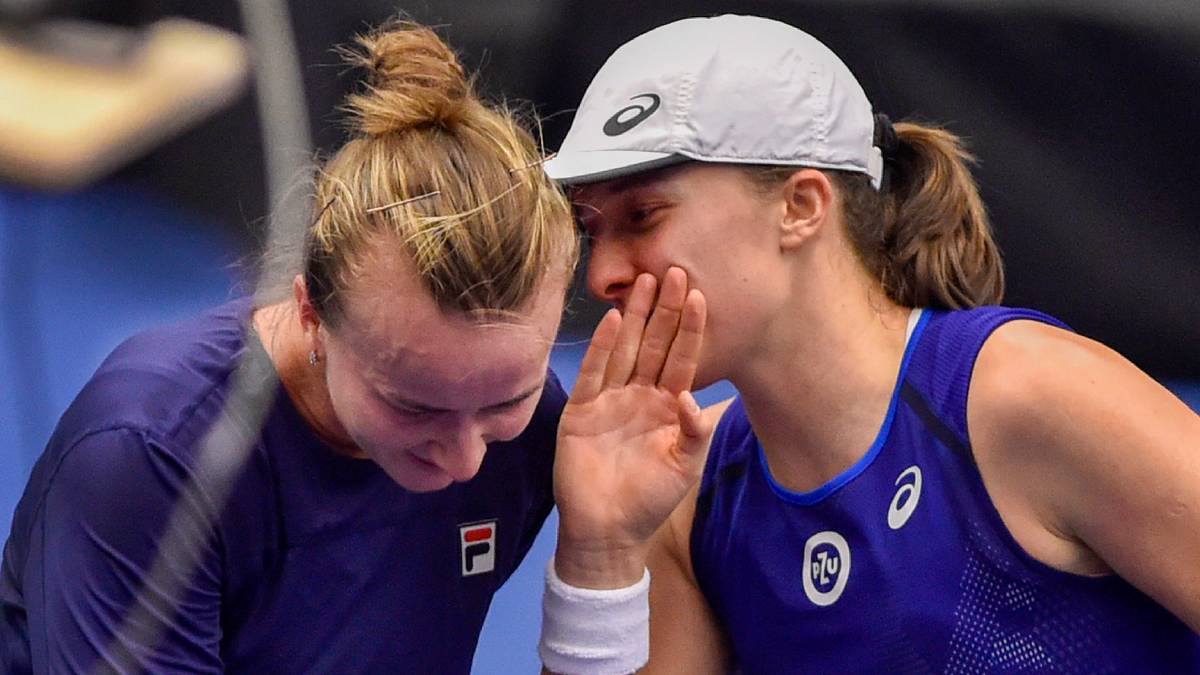 Dwie tenisistki dzielą się tajemnicą podczas gry.