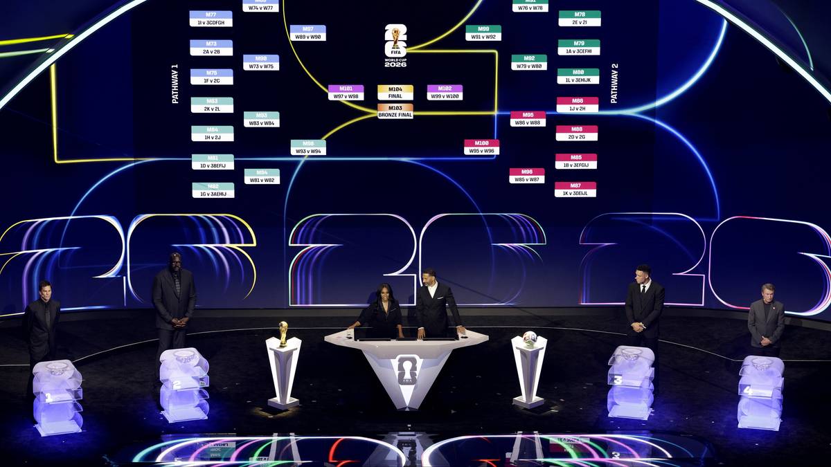 Drabinka turniejowa na ekranie podczas losowania, z ludźmi na scenie.