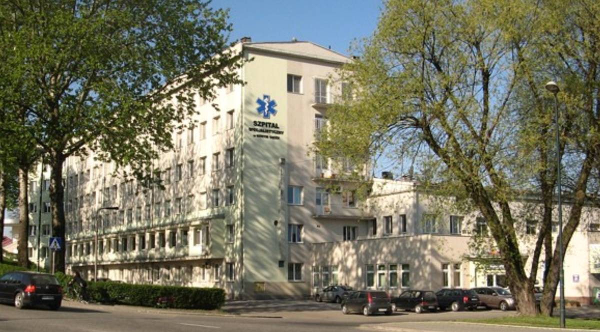 Budynek szpitala z parkingiem i drzewami wok&oacute;ł