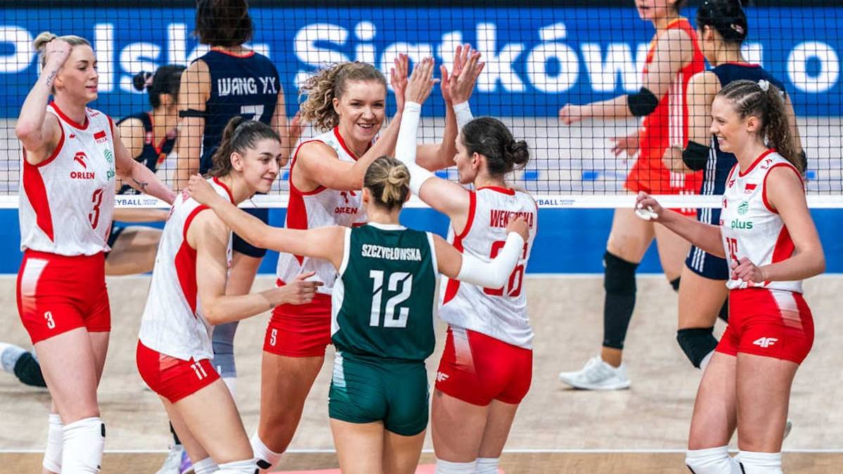 Grupa sportsmenek świętuje na boisku siatkarskim, niektóre z nich unoszą ręce w geście radości i klaszczą w dłonie.