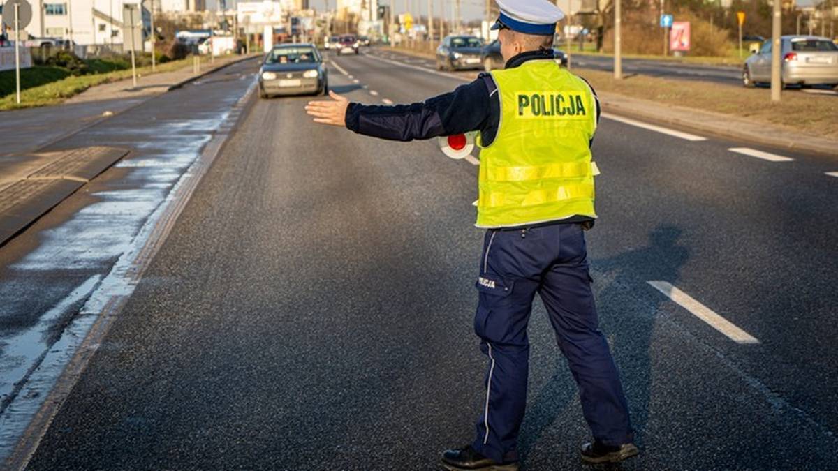 Policjant w kamizelce odblaskowej kieruje ruchem na drodze.