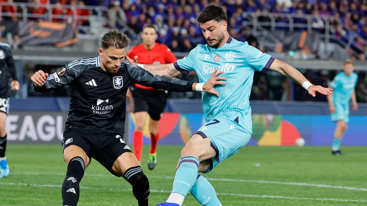 Piłkarz w czarnej koszulce pr&oacute;buje odebrać piłkę zawodnikowi w jasnoniebieskiej koszulce na boisku piłkarskim.