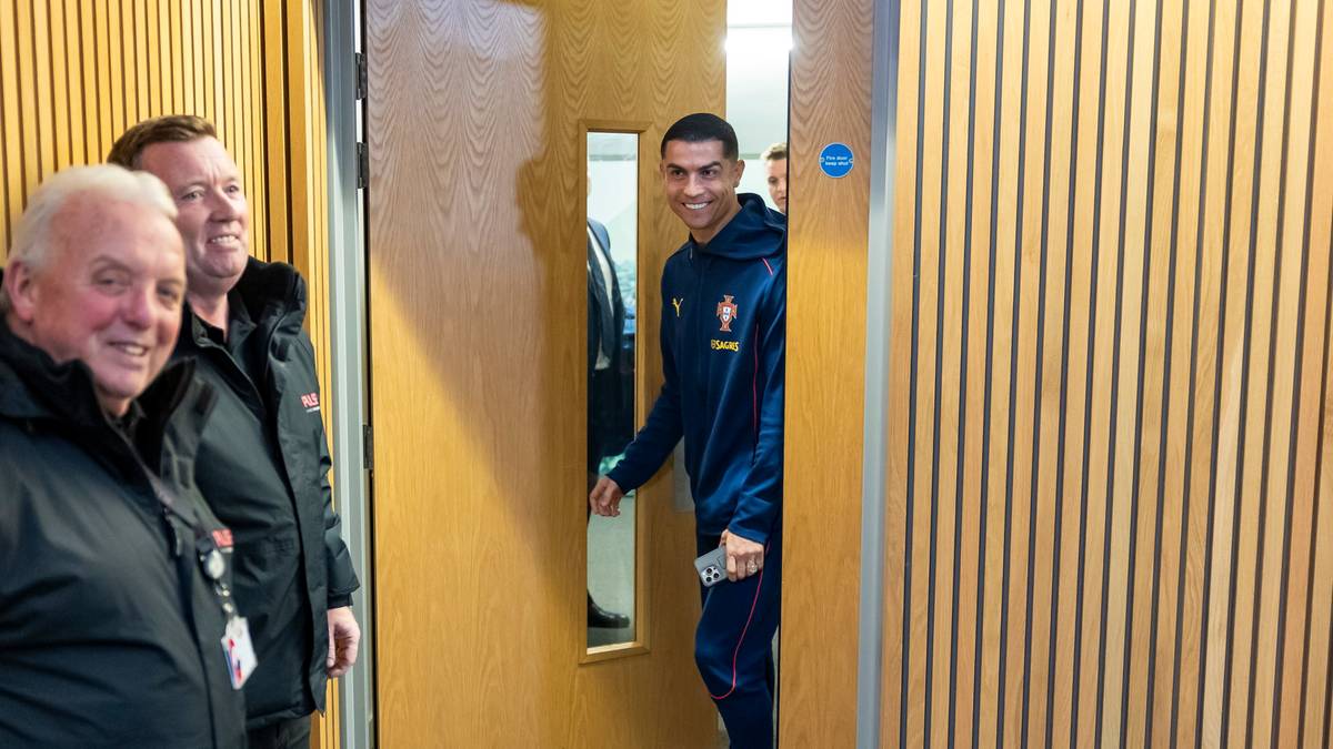 Cristiano Ronaldo w stroju reprezentacji Portugalii wychodzi zza drzwi, obok niego dwaj mężczyźni