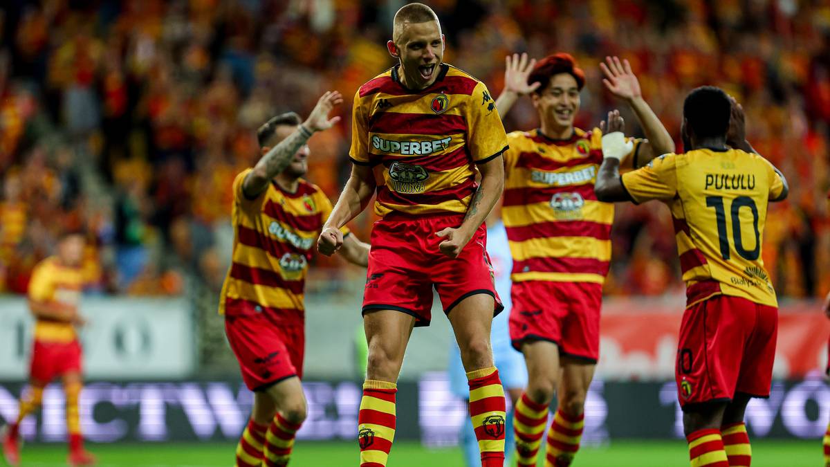 Piłkarze Jagiellonii Białystok w żółto-czerwonych strojach świętują bramkę, zdominantowani przez zawodnika z numerem 9 na plecach.