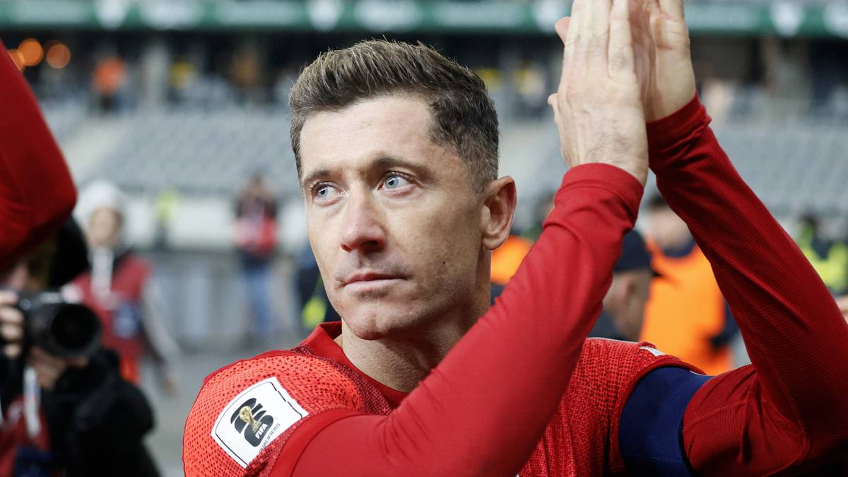 Piłkarz Robert Lewandowski w czerwonej koszulce z podniesionymi dłońmi nad głową, klaskający.