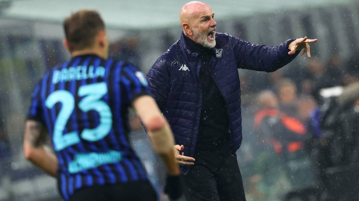 Trener piłkarski w niebieskiej kurtce, z siwą brodą i łysą głową, krzyczy i gestykuluje w stronę zawodnika.