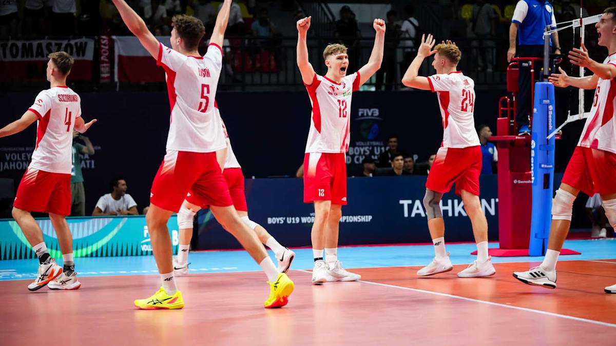 Grupa młodych siatkarzy w białych koszulkach z czerwonymi elementami i czerwonych spodenkach radośnie świętuje zdobycie punktu na parkiecie hali sportowej.