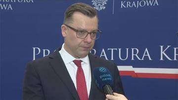 Mężczyzna w garniturze i okularach, przedstawiciel Prokuratury Krajowej, udziela wywiadu z mikrofonem Polsat News.