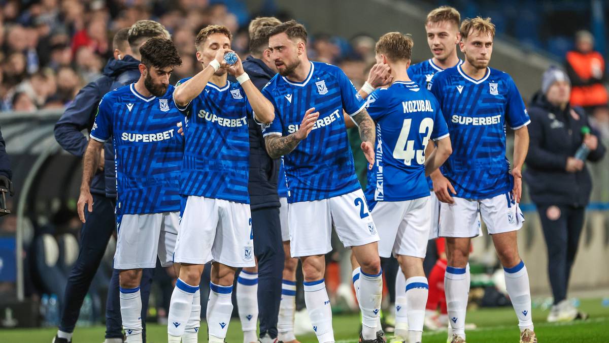 Piłkarze w niebieskich strojach stoją na boisku.