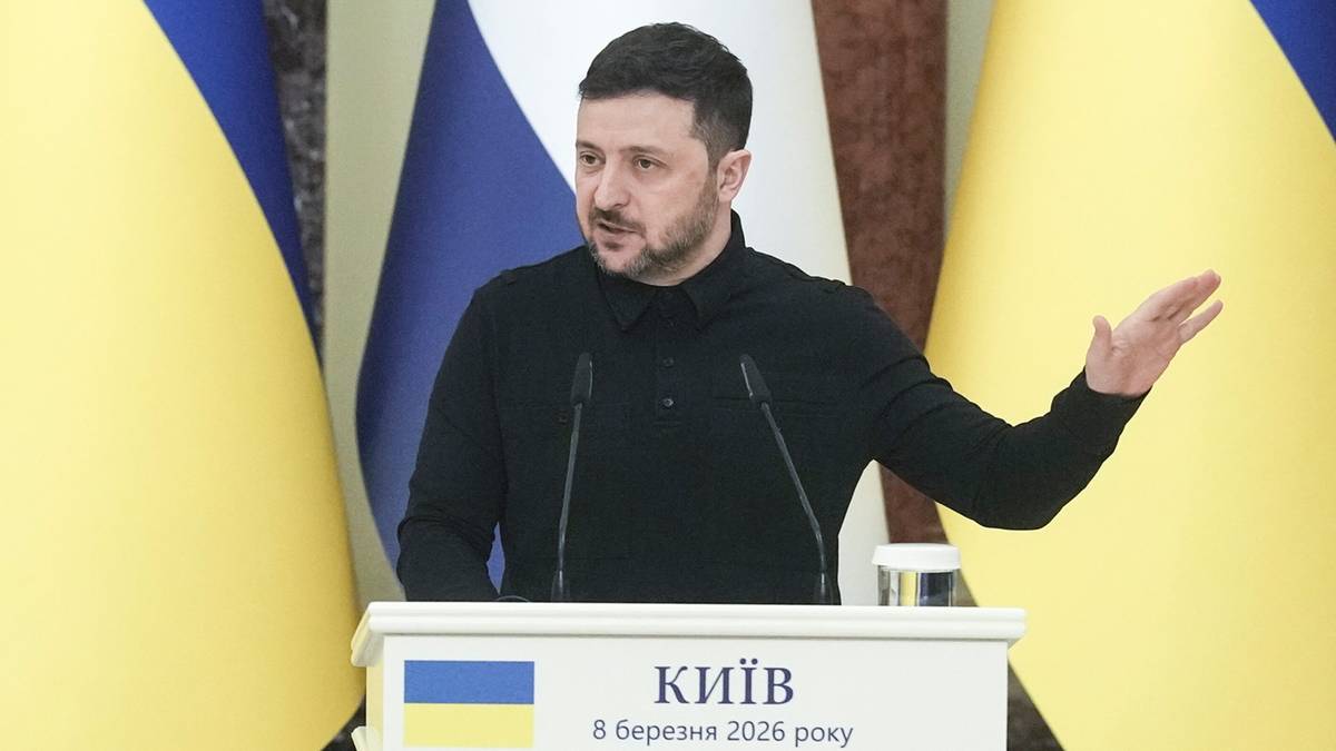 Prezydent Ukrainy Wołodymyr Zełenski przemawia za mównicą, na tle flag Ukrainy i innego państwa.