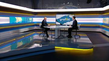 Dw&oacute;ch mężczyzn siedzi naprzeciwko siebie przy okrągłym stole w studiu telewizyjnym. Na ekranie za nimi wyświetlany jest napis "graffiti".
