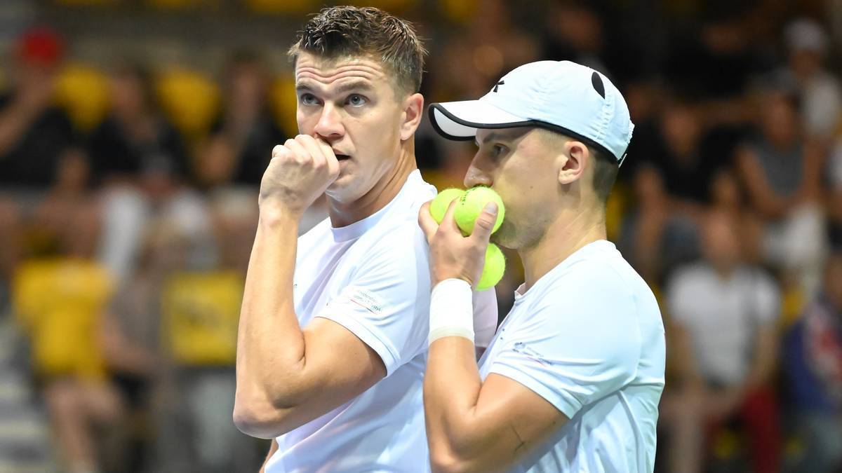 Dw&oacute;ch tenisist&oacute;w podczas meczu, jeden z nich trzyma piłki tenisowe.