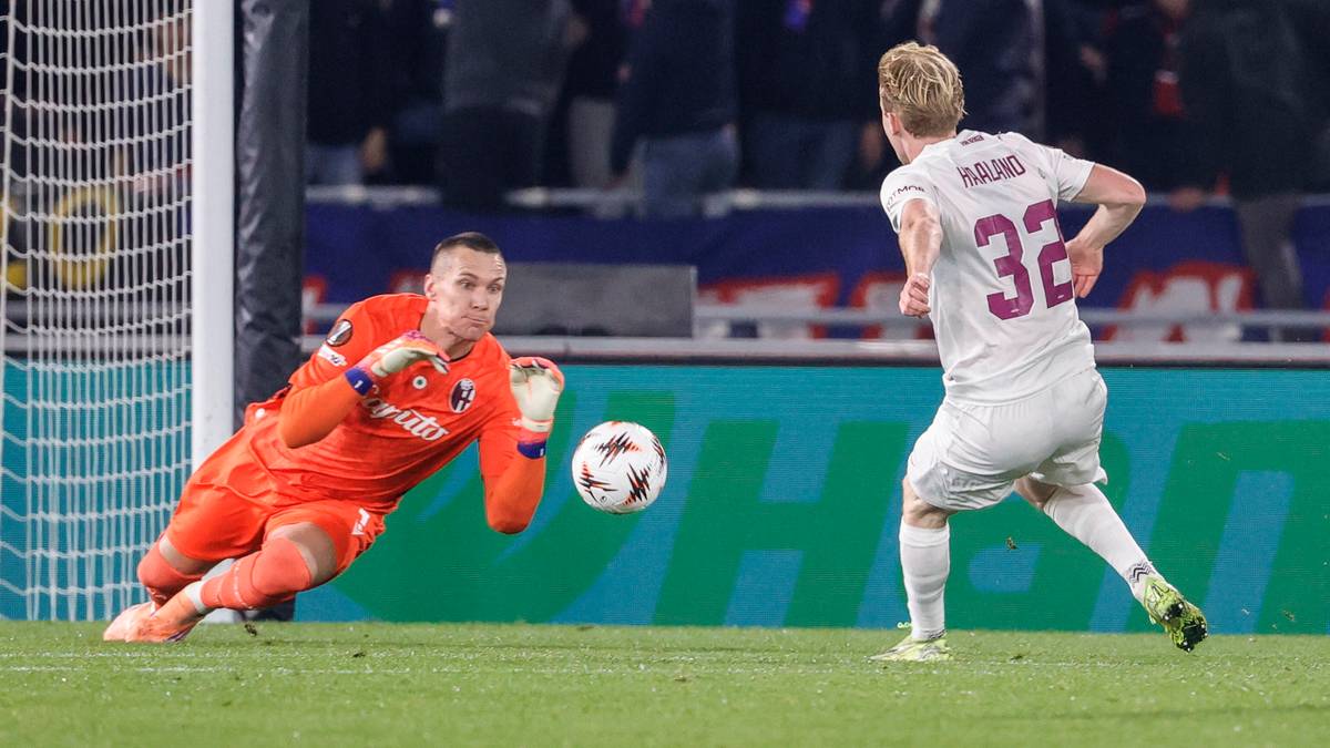 Bramkarz broni strzał piłkarza na boisku piłkarskim.