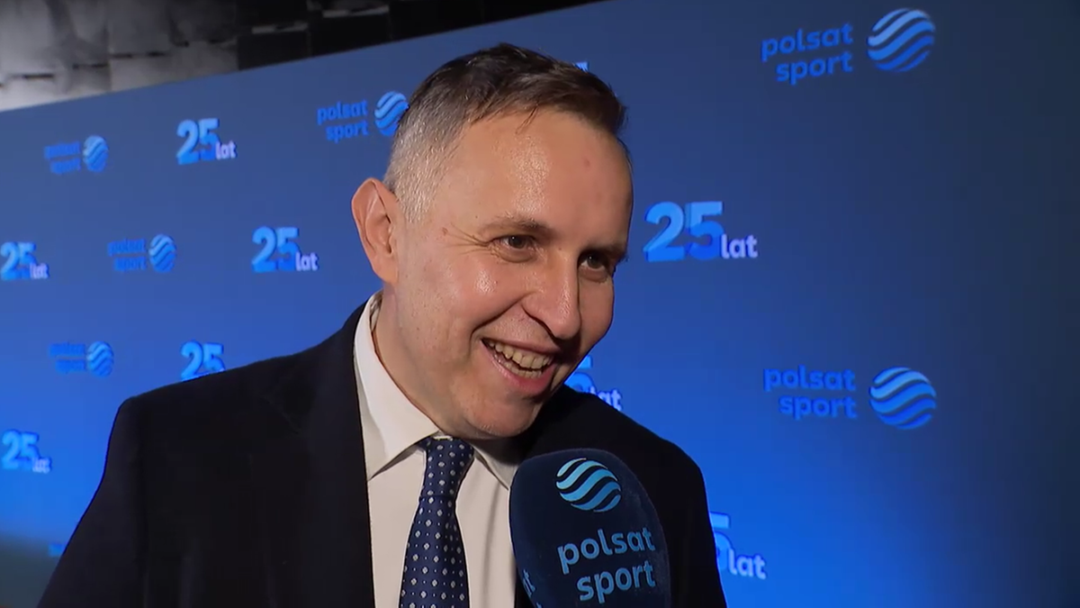 Roman Kołtoń, ubrany w garnitur i krawat, uśmiecha się, trzymając mikrofon Polsat Sport na tle niebieskiego banera z okazji 25-lecia stacji.