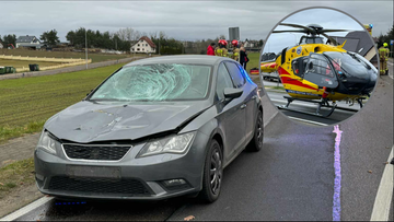 Szary samochód osobowy z pękniętą przednią szybą stoi na poboczu drogi. W prawym górnym rogu znajduje się wstawka ze zdjęciem żółtego śmigłowca Lotniczego Pogotowia Ratunkowego na pasie startowym.