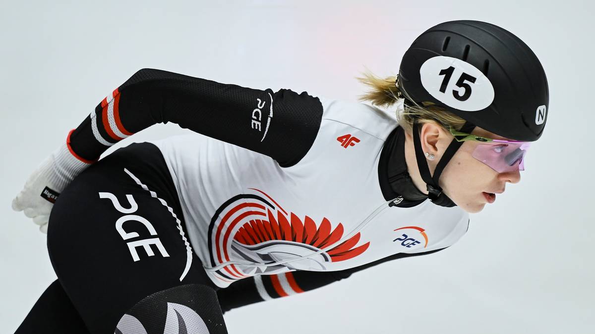 Zawodniczka short tracku w kasku i okularach ochronnych, pochylona w pozycji wyścigowej na lodzie.