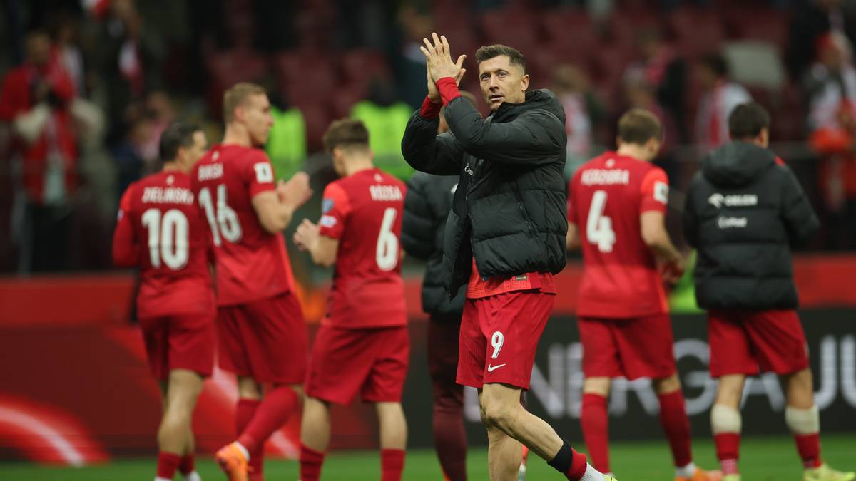 Piłkarze reprezentacji Polski w czerwonych strojach, w tym Robert Lewandowski, klaszczą na boisku.