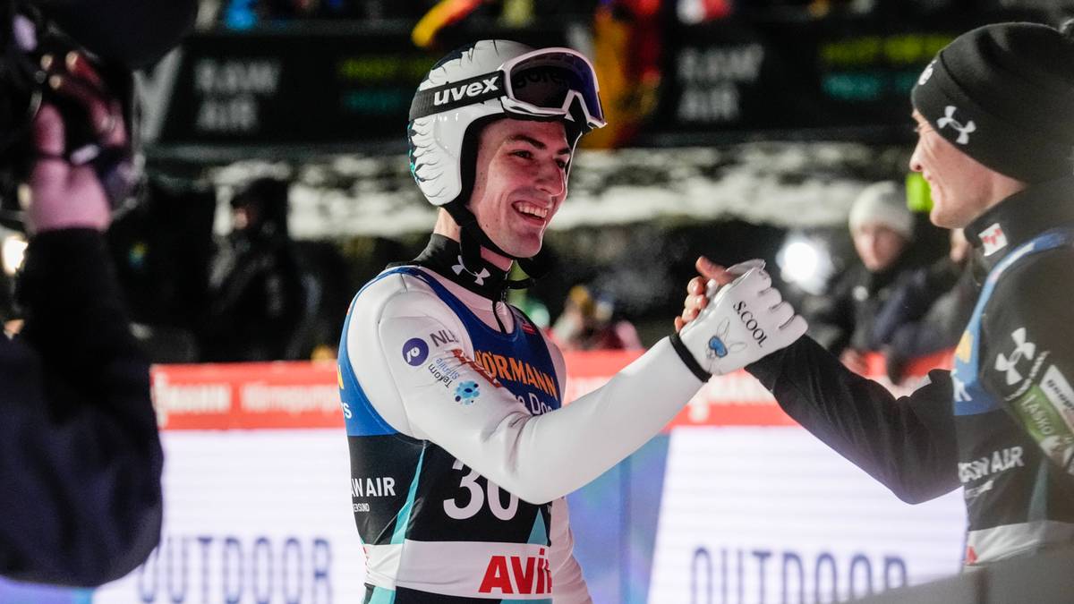 Młody sportowiec w kasku i goglach narciarskich, uśmiechnięty, podaje rękę innemu zawodnikowi.