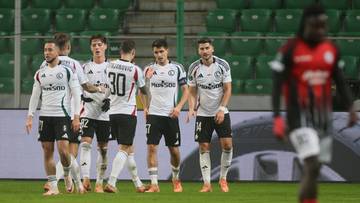 Piłkarze Legii Warszawa w białych strojach świętują bramkę na tle zielonych trybun.