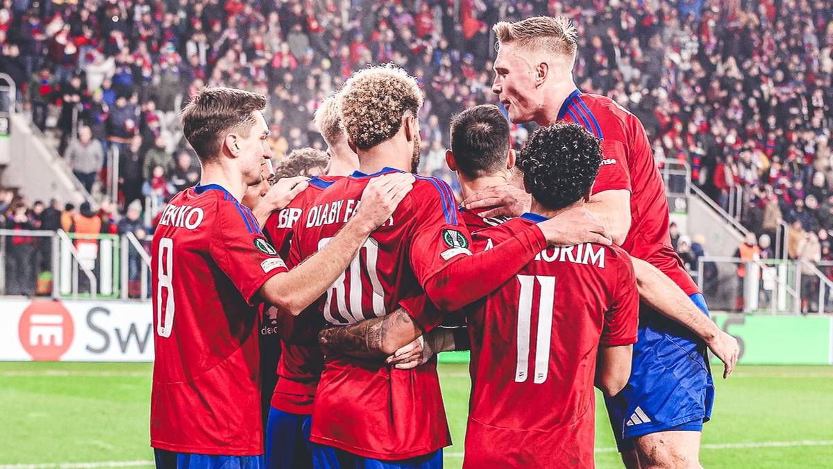 Piłkarze w czerwonych koszulkach świętują zdobycie bramki, przytulając się na boisku.