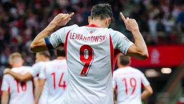 Robert Lewandowski w białej koszulce reprezentacji z numerem 9, świętujący bramkę z uniesionymi palcami.