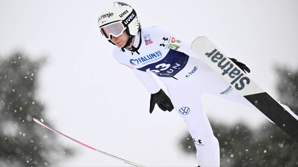 Skoczek narciarski w białym kombinezonie i kasku podczas skoku.