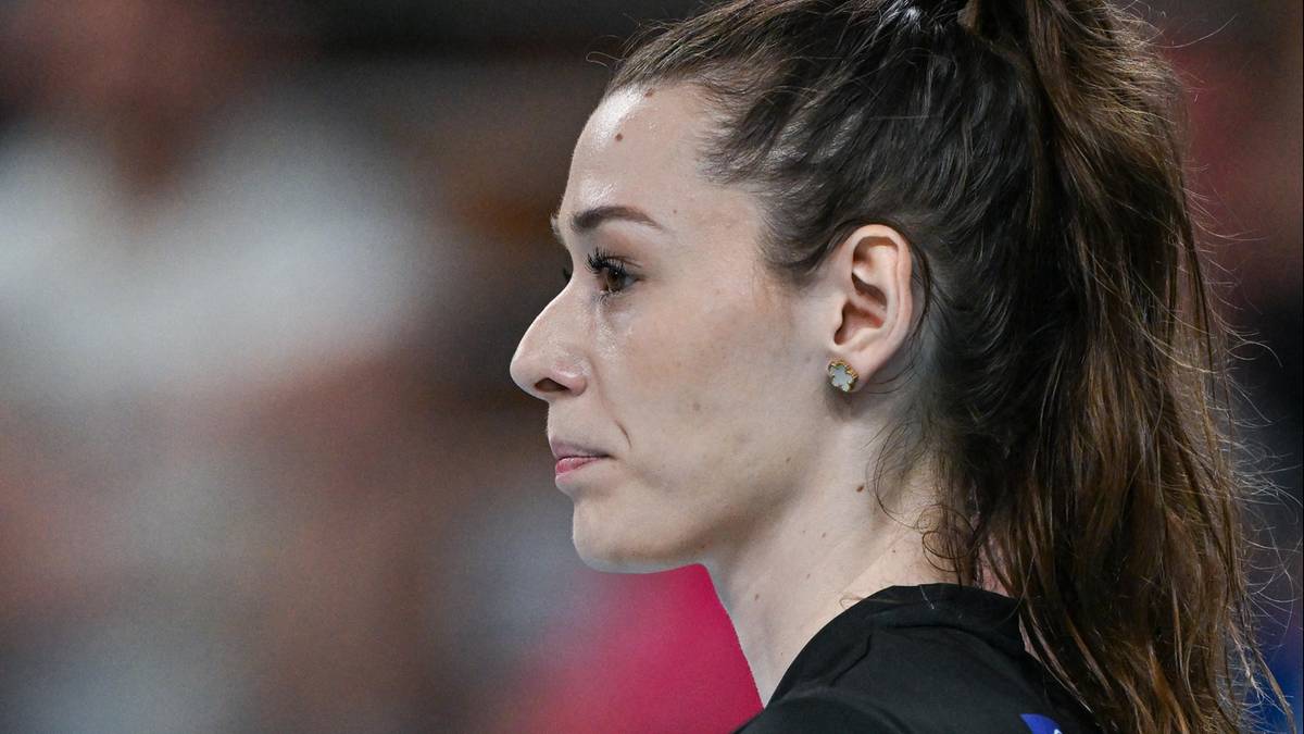 Siatkarka w czarnej koszulce z numerem 9 trzyma piłkę do siatkówki, patrząc w bok.