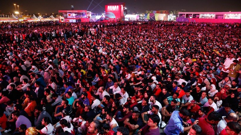 Ogromny tłum ludzi siedzi na ziemi, oglądając transmisję meczu na ekranie na nocnym wydarzeniu sportowym.