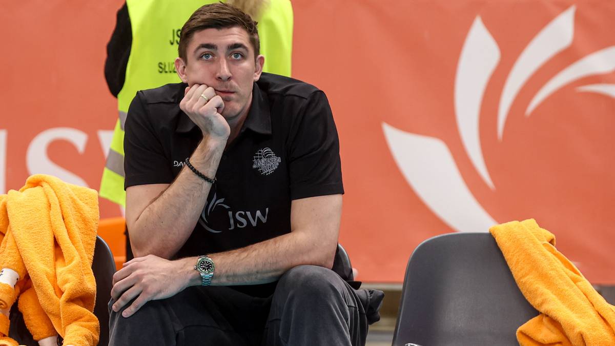 Mężczyzna w koszulce z napisem JSW, siedzący i zamyślony.